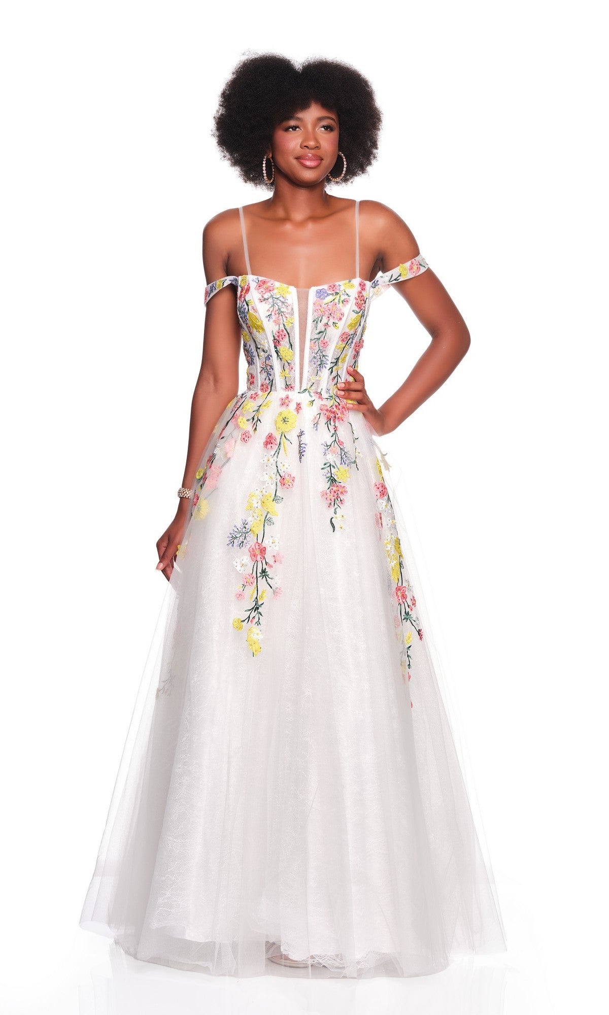 A woman wears the Dave and Johnny 12489 long prom dress featuring white floral embroidery, off-the-shoulder straps, and a sheer tulle overlay, standing against a white background.